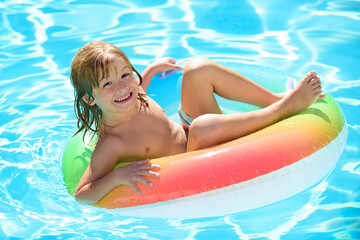 Kids Swimming with Swim Ring. Happy kid playing with colorful swim ring in swimming pool on summer day. Child water toys. Children play in tropical resort. Family beach vacation.
