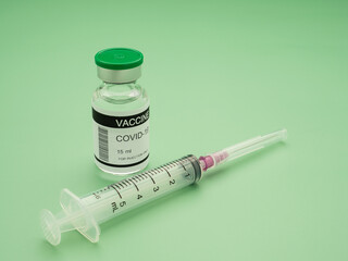 Close-up of a Covid-19 vaccine in glass bottle and syringe placed on a green background. Vaccine for prevention, immunization, and treatment from coronavirus infection. Concept of medical