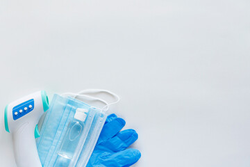 Corona virus protection concept flat lay. Non-contact infrared body thermometer, latex gloves, disposable masks and sanitizer on white background with copy space.
