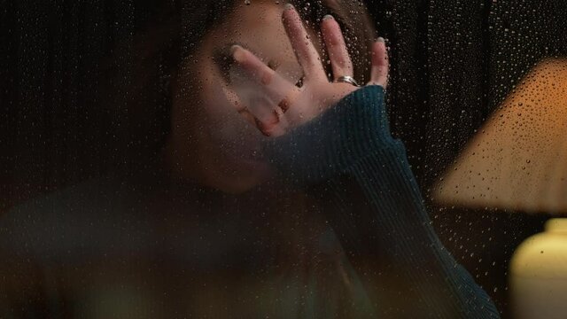 Close up of young woman drawing a heart on glass during a rainy night at home