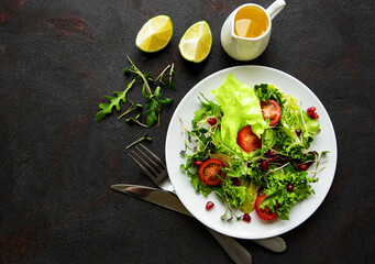Fresh green mixed  salad bowl with tomatoes and microgreens  on black concrete background. Healthy food, top view.