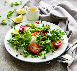 Fresh green mixed  salad bowl with tomatoes and microgreens  on  concrete background. Healthy food, top view.