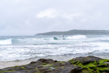 Fototapeta na wymiar Male man catching waves surfing at Maroubra beach on a wet winters day, cloudy day, overcast