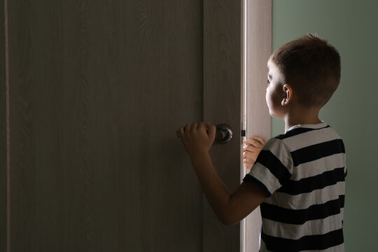 Little Boy Peeking Through Open Door In Dark Room