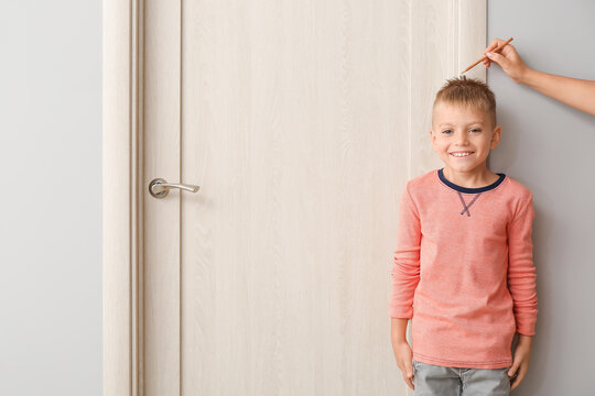 Female hand with pencil and cute little boy measuring height near closed door