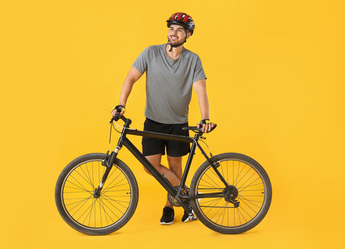 Male cyclist with bicycle on color background