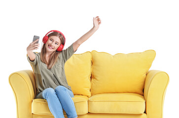 Happy young woman with mobile phone and headphones on sofa against white background