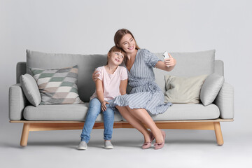 Mother and daughter taking selfie on sofa against light background