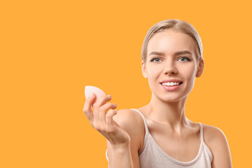 Beautiful young woman with makeup sponge on color background