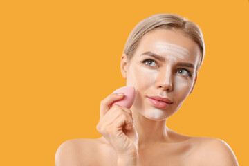 Beautiful young woman applying contouring makeup against color background