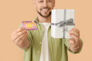 Handsome man with gift card and present on color background