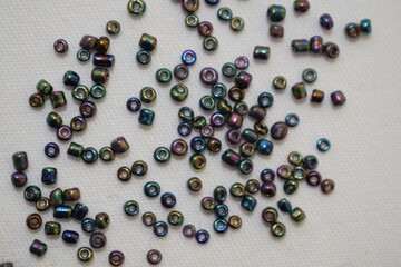 Dark beads scattered on a white background. Materials for needlework.
