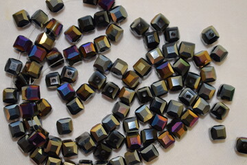 Dark square beads scattered on a white background. Materials for needlework.