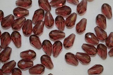 Burgundy beads in the form of a drop scattered on a white background. Materials for needlework.