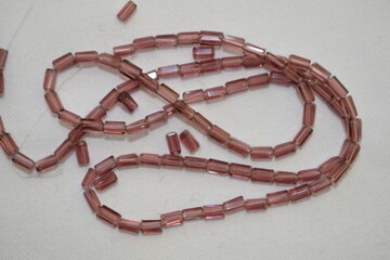 Burgundy beads in the form of a cylinder scattered on a white background. Materials for needlework.