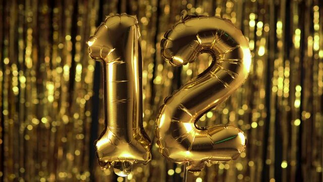 Gold foil number 12 twelve festive balloon on a yellow background. The concept of birthday, anniversary, date.