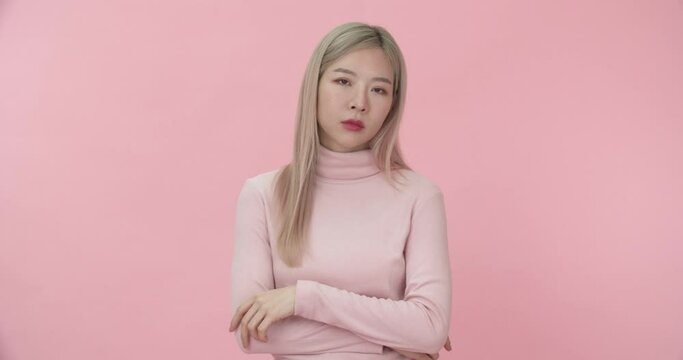 Portrait of young beautiful Asian woman in pink long sleeve t-shirt cross arms on chest and sulking offended, feeling mad, looking at the camera on pink background. Emotion and Body language concept.