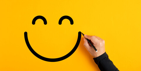 Male hand drawing a smiling happy face sketch on yellow background. Client satisfaction, service or product evaluation - obrazy, fototapety, plakaty