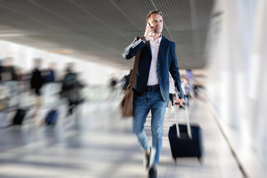 Man walking in airport carrying hand luggage while talking on phone