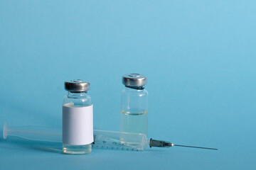 Two vials of vaccine and a medical syringe close-up on a blue isolated background. The concept of...