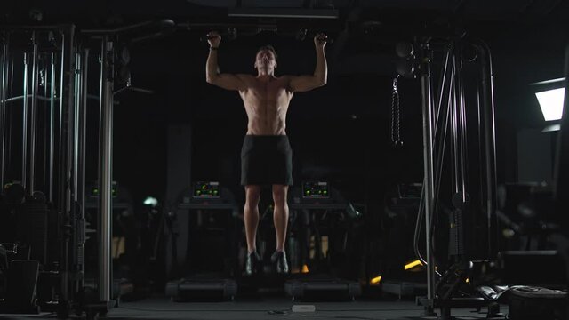 Wellness, athletic man performs pull-ups on the horizontal bar, strength training in the gym at night, cinematic light, 4k 50fps.