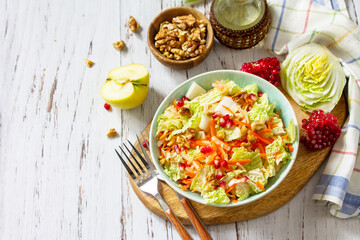 Dietary salad fresh vegetable of Chinese cabbage, carrots, apple, nuts and pomegranate with vinaigrette dressing on a white wooden table. Copy space.