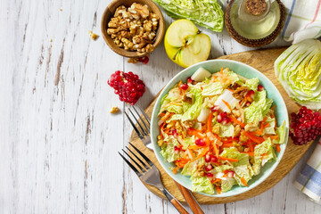 Dietary salad fresh vegetable of Chinese cabbage, carrots, apple, nuts and pomegranate with vinaigrette dressing on a white wooden table. Top view flat lay. Copy space.