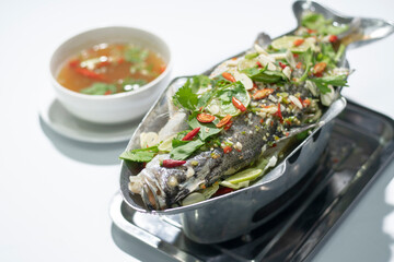 Plate of steamed Giant perch. Steamed fish with spicy lemon sauce on white background, Selective focus. Thai seafood for advertising ideas concept.