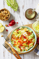 Dietary salad fresh vegetable of Chinese cabbage, carrots, apple, nuts and pomegranate with vinaigrette dressing on a white wooden table. Top view flat lay.