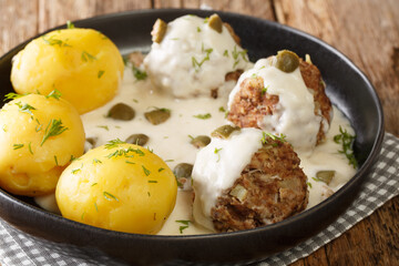 Delicious German meatballs in caper sauce served with boiled potatoes close-up in a plate on the table. Horizontal