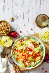 Dietary salad fresh vegetable of Chinese cabbage, carrots, apple, nuts and pomegranate with vinaigrette dressing on a white wooden table. Top view flat lay. Copy space.