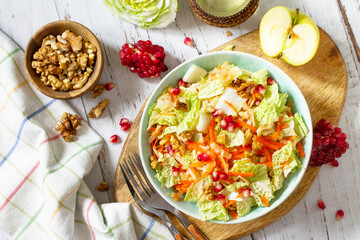 Dietary salad fresh vegetable of Chinese cabbage, carrots, apple, nuts and pomegranate with vinaigrette dressing on a white wooden table. Top view flat lay.