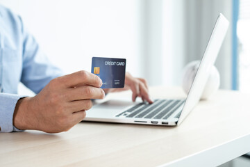 The businessman's hand is holding a credit card and using a laptop for online shopping and internet payment in the office