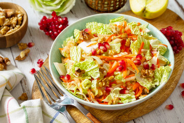 Dietary salad fresh vegetable of Chinese cabbage, carrots, apple, nuts and pomegranate with vinaigrette dressing on a white wooden table.