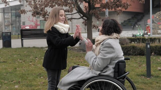Disabled woman in wheelchair with her daughter walking together and playing outdoors. For people with disabilities. Family concept.