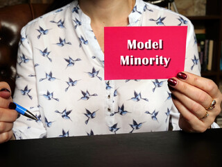 Blank pink business card in a hand with phrase Model Minority . Horizontal shot. Close-up