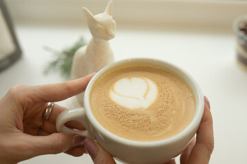 Close up of beautiful female hands holding big white cup of cappuccino coffee. Selective focus.