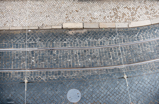 Lisbon cobblestone street aerial with tram tracks and wires.