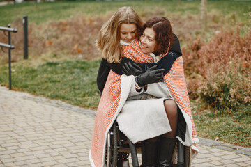 Disabled woman in wheelchair with daughter. Family walking outside at park. Little girl covered her...
