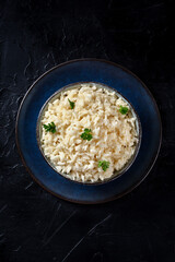 Rice, boiled, served with fresh parsley leaves, shot from the top on a dark background with copy space