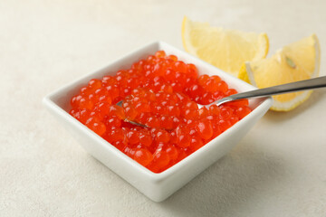 Bowl with caviar and spoon, and lemons on white textured background