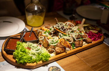 mixed meat with salad and sauce on a board with lemonade for company on a table, horizontal