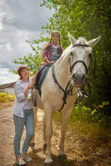 A teenage girl, mother and a horse in nature among green trees