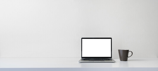 Modern contemporary workspace with blank screen laptop computer and coffee cup on office desk table on white background for copy space. Home office workplace concept.