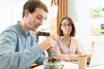 A handsome man chatting with a coworker while eating a salad. Healthy nutrition habits in the office concept.