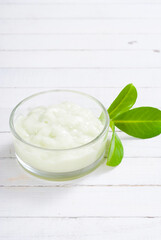 cosmetic cream in glass pot and leaves on white wood