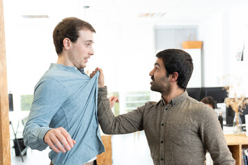 Angry hispanic man fighting and threatening a frightened caucasian coworker at the office.