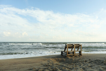 Fototapeta na wymiar Wooden bench on sandy sea beach, space for text