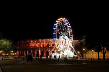 an illuminated ferris wheel in front of the Arenes de Nimes in Occitanie, France, November