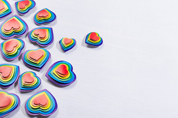 Lgbt love background - rainbow hearts on white wood board, border, top view.